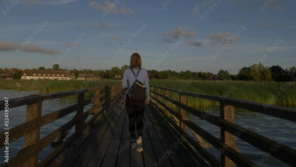 Woman walks at sunset over lagoon pier in Slowinski National Park in Poland. Woman walks at sunset over lagoon pier in Slowinski National Park in Poland.