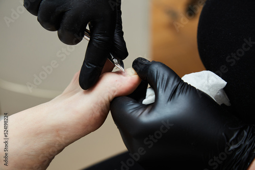 The manicure and pedicure master removes the cuticle on the toe in the pedicure salon. Black gloves on his hands. Foot care procedure  decorative design on the feet.