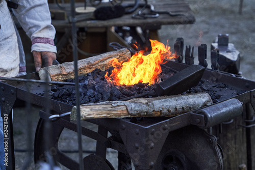 Blazing bright fire in the iron forge basin of the blacksmith filled with charcoal, wood and tools