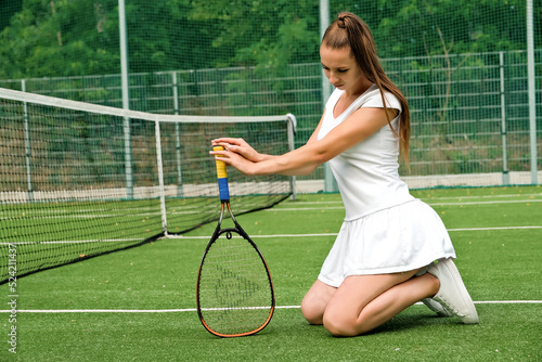 a girl in a white sports dress sits on a tennis court. tennis court and racket.