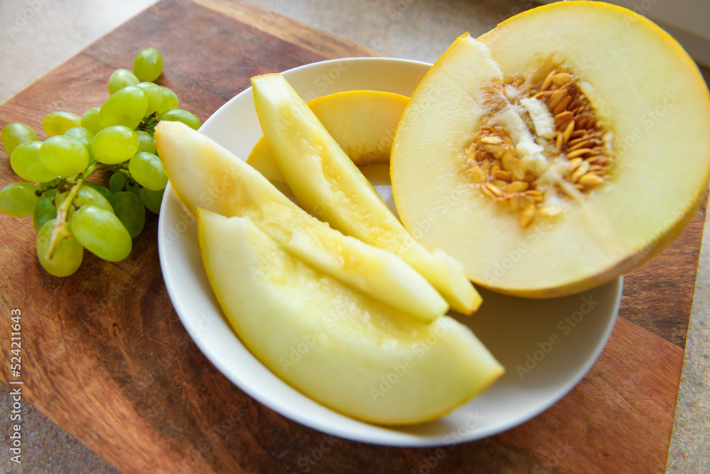 sliced melon with seeds on a white plate, green grapes on a wooden board, the concept of fresh fruit and healthy eating
