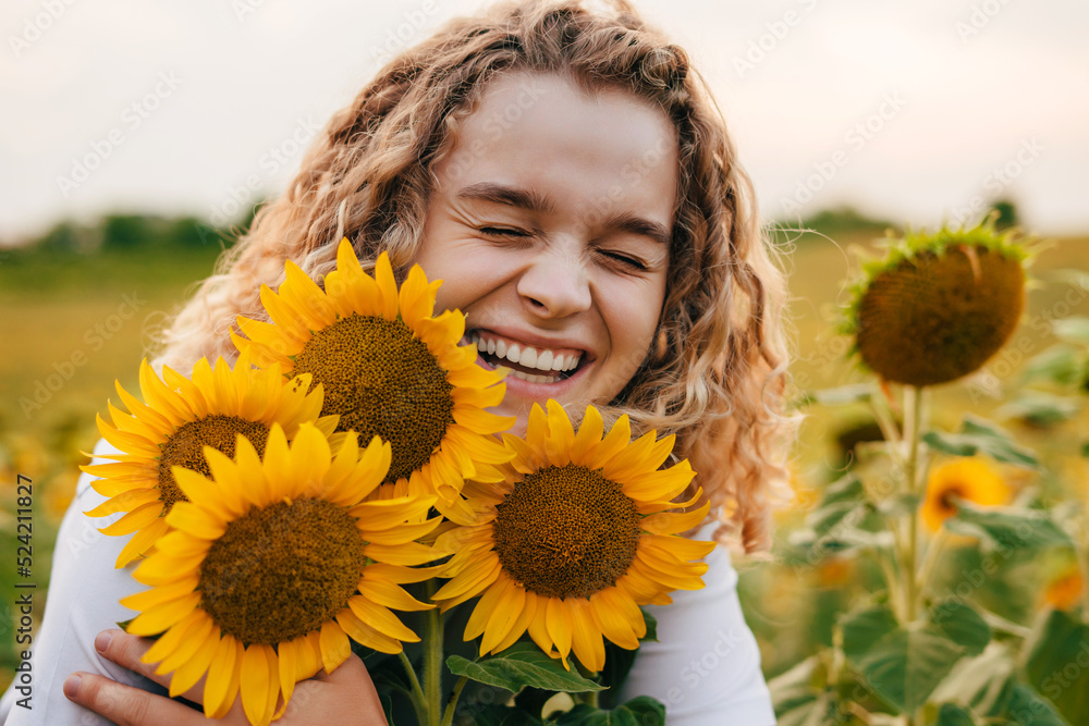 Happy curly girl embracing sunflower flowers in a field of sunflowers at sunset. Beauty portrait. Natural summer landscape. Agronomist and farmer inspect Happy curly girl embracing sunflower flowers in a field of sunflowers at sunset. Beauty portrait. Natural summer landscape. Agronomist and farmer inspect