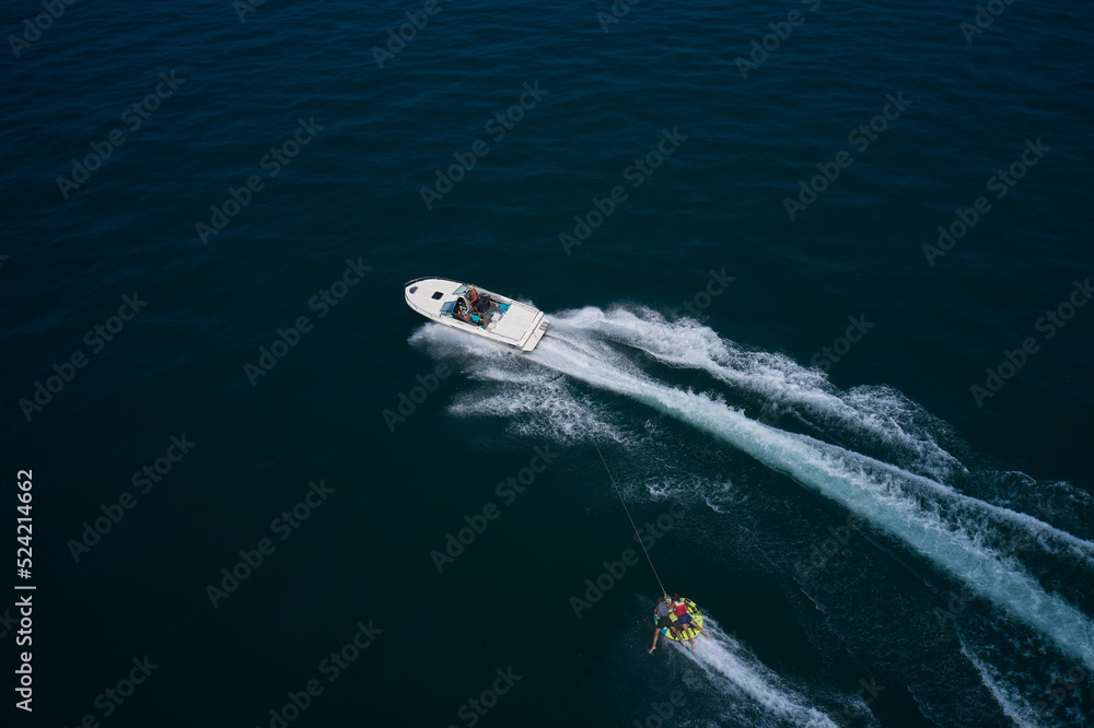 A white big boat pulls a tubing with two people aerial view. tubing boat top view. Yellow tubing boat with people in motion aerial view. Attractions on the water.