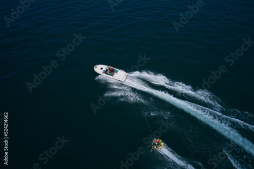 A white big boat pulls a tubing with two people aerial view. tubing boat top view. Yellow tubing boat with people in motion aerial view. Attractions on the water. © Berg