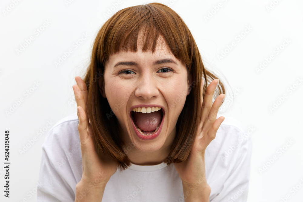 a close horizontal studio photo of a red-haired woman screaming loudly clutching her head from shock. a close horizontal studio photo of a red-haired woman screaming loudly clutching her head from shock.