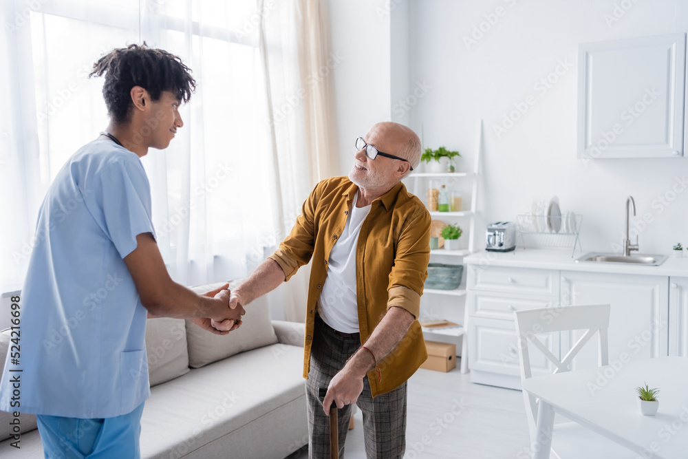 Smiling elderly patient with walking cane shaking hand of african american nurse at home. Smiling elderly patient with walking cane shaking hand of african american nurse at home.