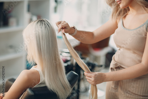 Obraz na płótnie Hairdresser female making hair extensions to young woman with blonde hair in beauty salon. Professional hair extension w salonie