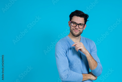Young Handsome Caucasian Man in Glasses With Folded Hands Looking Straight And Smiling Against Seamless Blue Background.