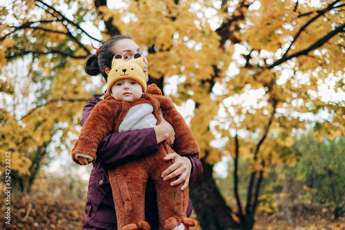 A woman walks in the park in autumn with her child. A young woman holds her baby in her arms and stands under a tree.