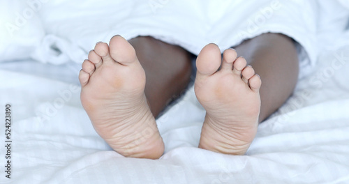 Black woman bare-feet take a rest in bed. African American female legs.