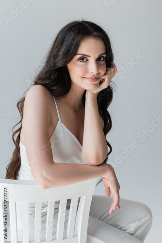 Portrait of pretty woman in white clothes sitting on chair isolated on grey.