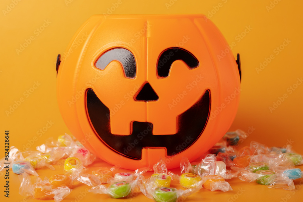Fototapeta premium Halloween pumpkin candy bowl with different lollipops on orange background, Halloween party