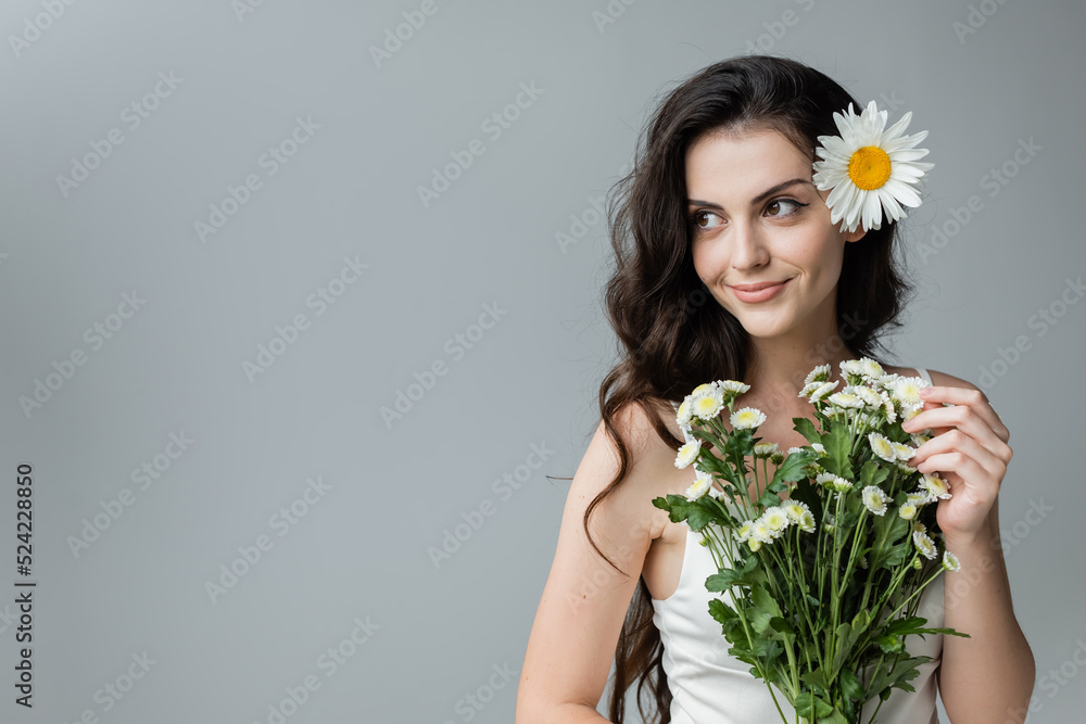 Smiling young woman holding bouquet of chamomiles isolated on grey. Smiling young woman holding bouquet of chamomiles isolated on grey.