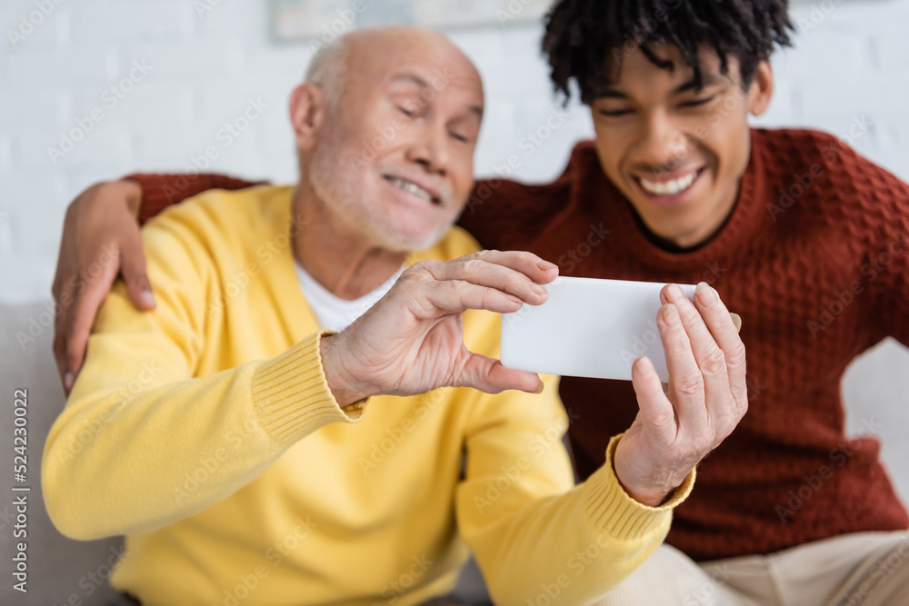 Smartphone in hands of blurred pensioner near african american grandson at home. Smartphone in hands of blurred pensioner near african american grandson at home.
