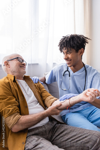 Smiling african american nurse holding cotton pad on hand of senior patient at home.