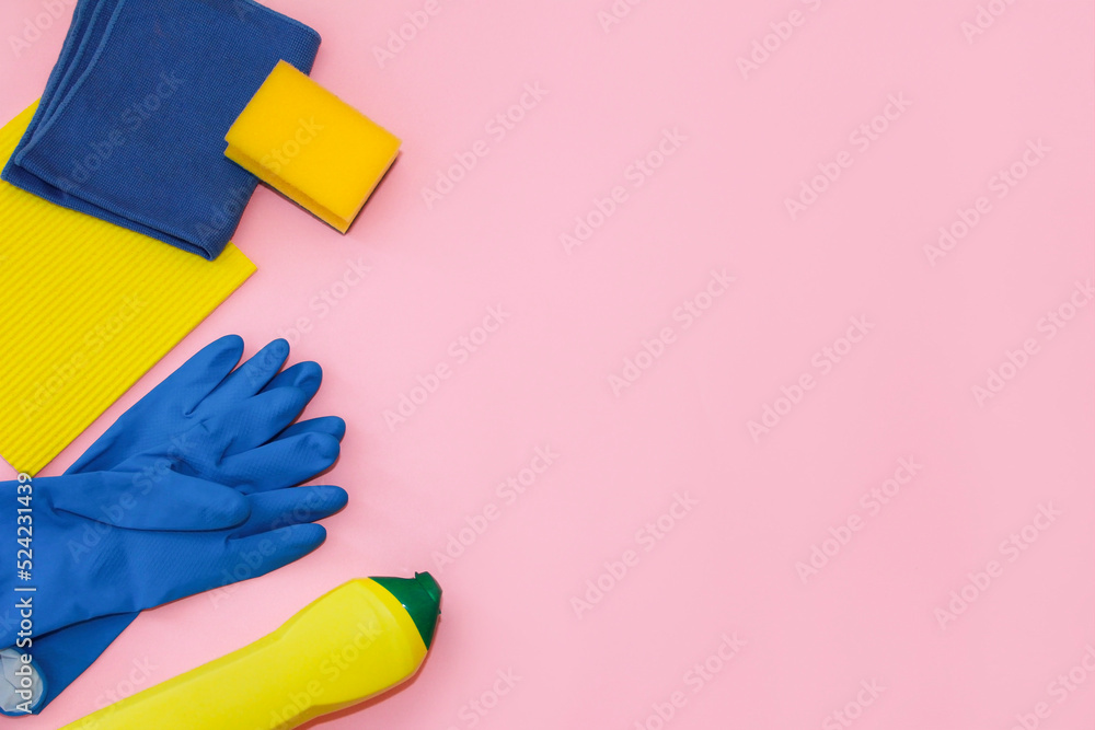 household cleaning supplies, yellow and blue rag, foam sponge, rubber gloves and cleaning cream in a yellow bottle, on a pink background household cleaning supplies, yellow and blue rag, foam sponge, rubber gloves and cleaning cream in a yellow bottle, on a pink background