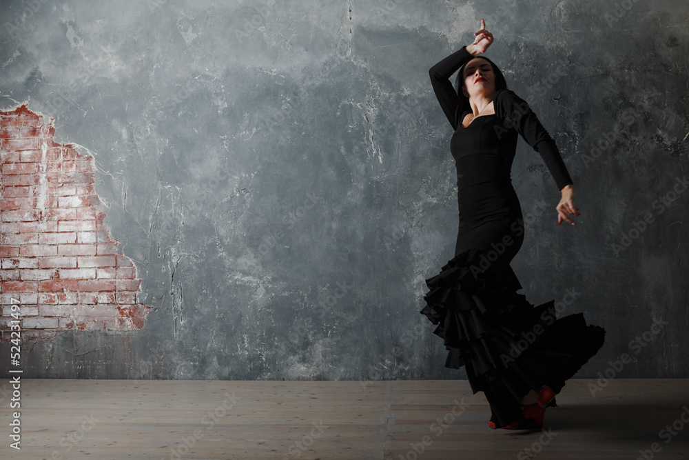 Fototapeta premium Young adult spanish woman dancing flamenco on gray vintage studio background