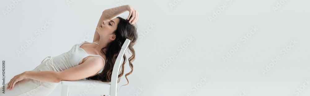 Side view of long haired model posing near chair isolated on grey, banner. Side view of long haired model posing near chair isolated on grey, banner.
