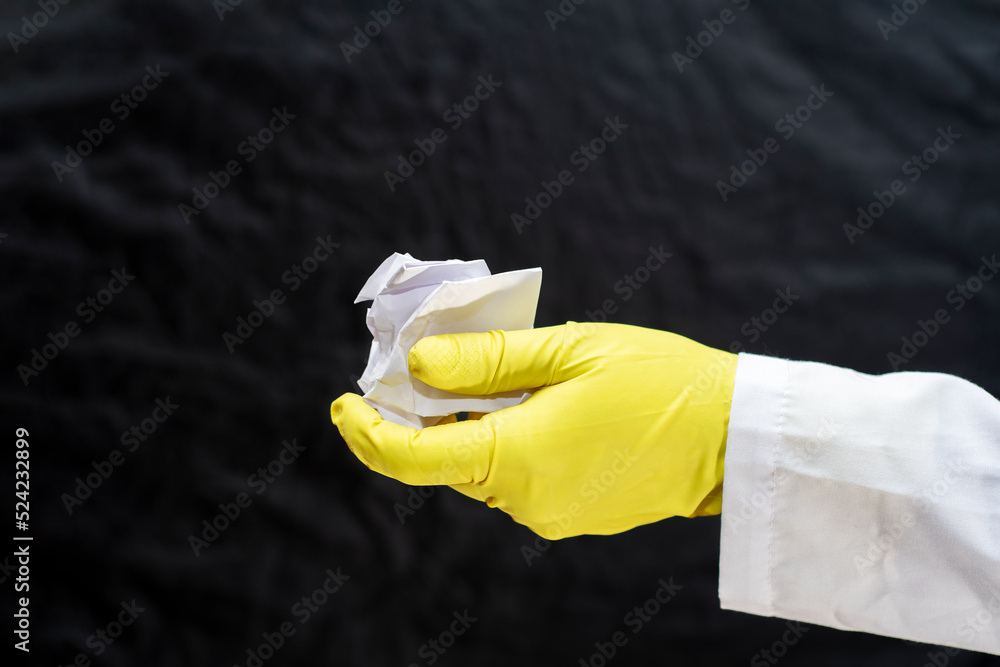 A doctor in a medical gown and protective gloves holds a crumpled sheet of paper in his hand. The face is not visible. Concept - pollution with waste and garbage.