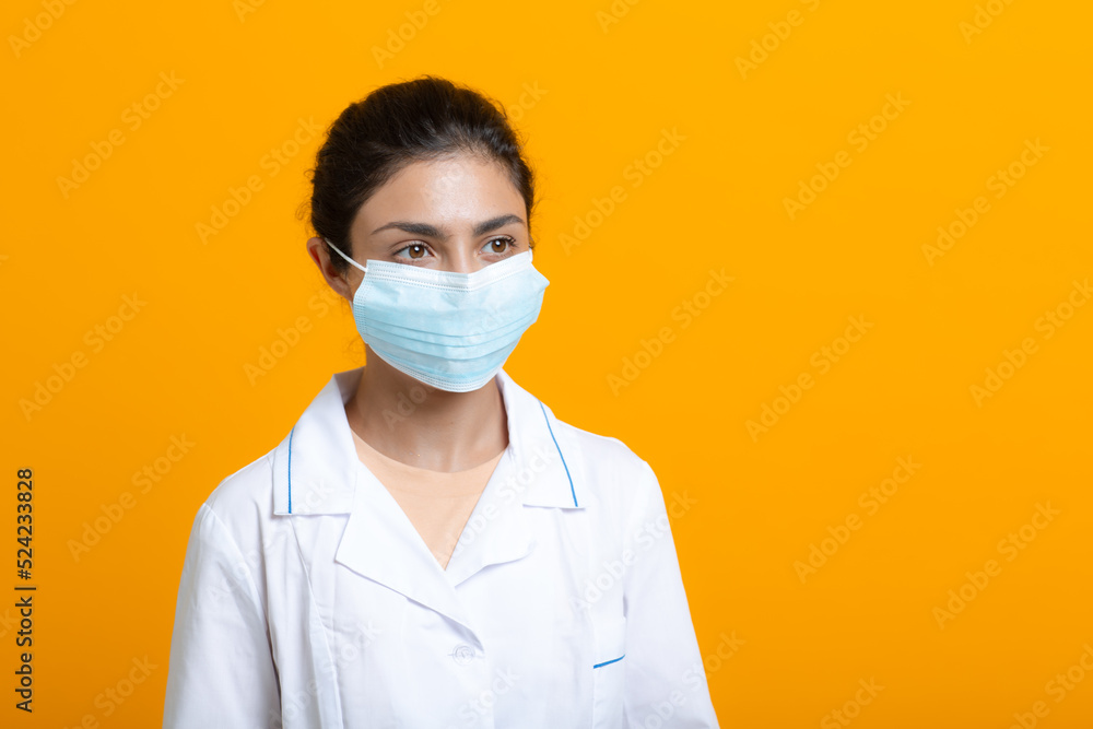 Portrait of indian doctor woman wearing white medical gown and face mask isolated on yellow background. Portrait of indian doctor woman wearing white medical gown and face mask isolated on yellow background.