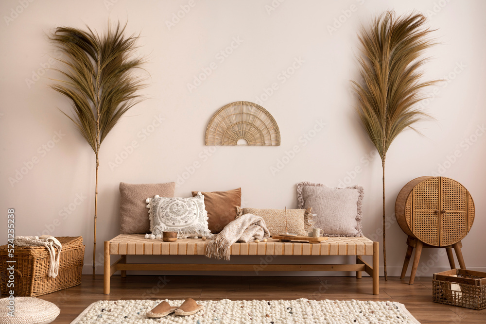 Boho and cozy interior of meditation room with beige chaise lounge, carpet,  rattan commode, pillows, side table, decoration, books, carpet and personal  accessories. Warm home decor. Template. Stock Photo