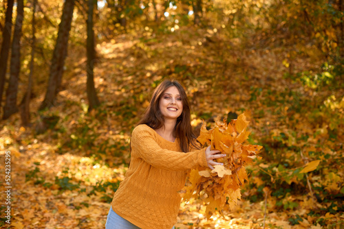 smiling caucasian woman in yellow sweater throwing autumn leaves laughing in colorful forest foliage