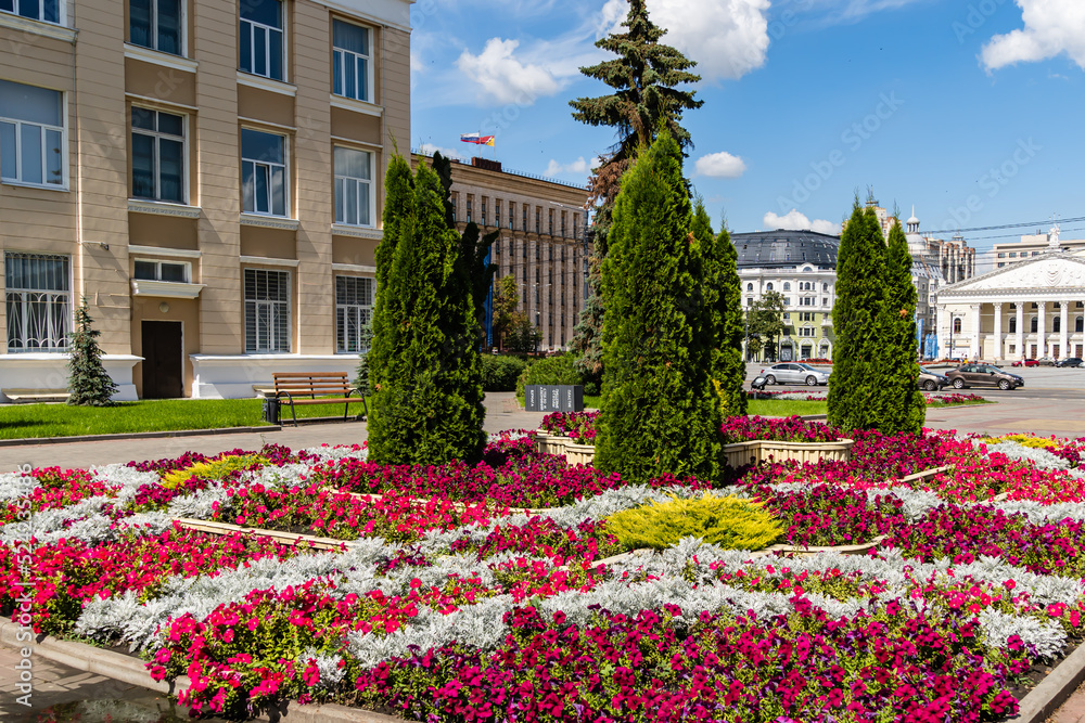 Beautiful flowerbed of purple and red flowers with evergreens in  center. City center. Lenin Square. In background is Opera and Ballet Theatre. Voronezh, Russia - July 30, 2022