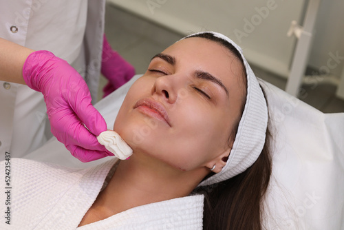 Close up face of thread lifting procedure. Professional cosmetologist in pink medical gloves inserting needles in chin scin. Anti-aging treatment and face lift in cosmetology clinic. Pretty woman face