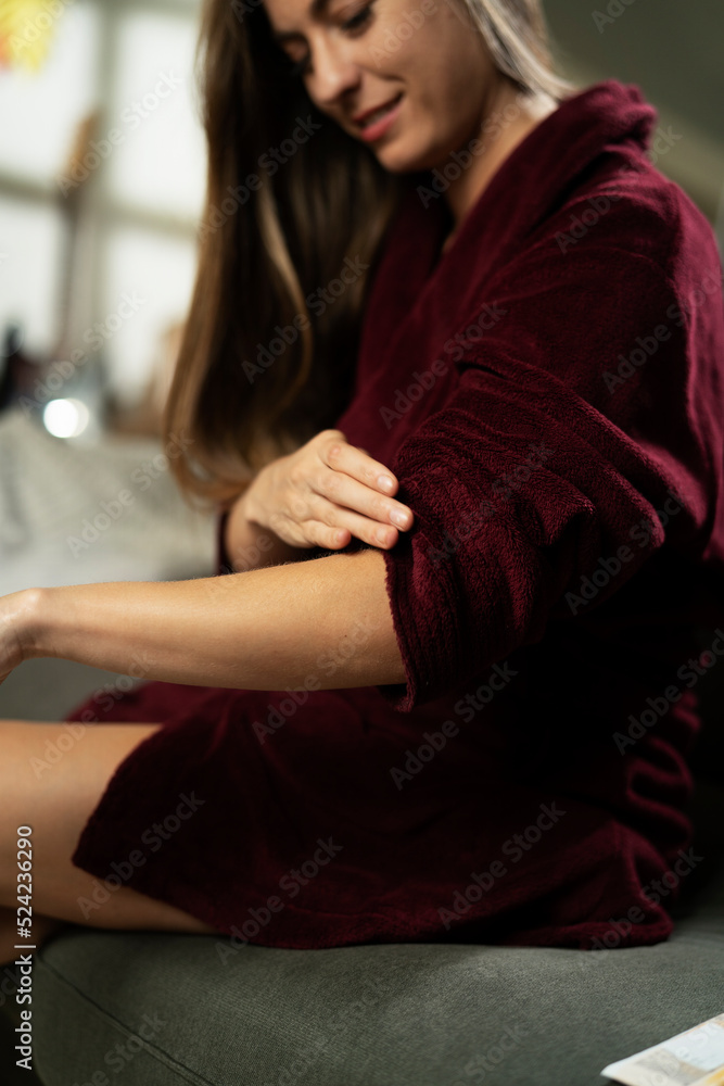 Woman applying body cream on her hand in living room.. Woman applying body cream on her hand in living room..