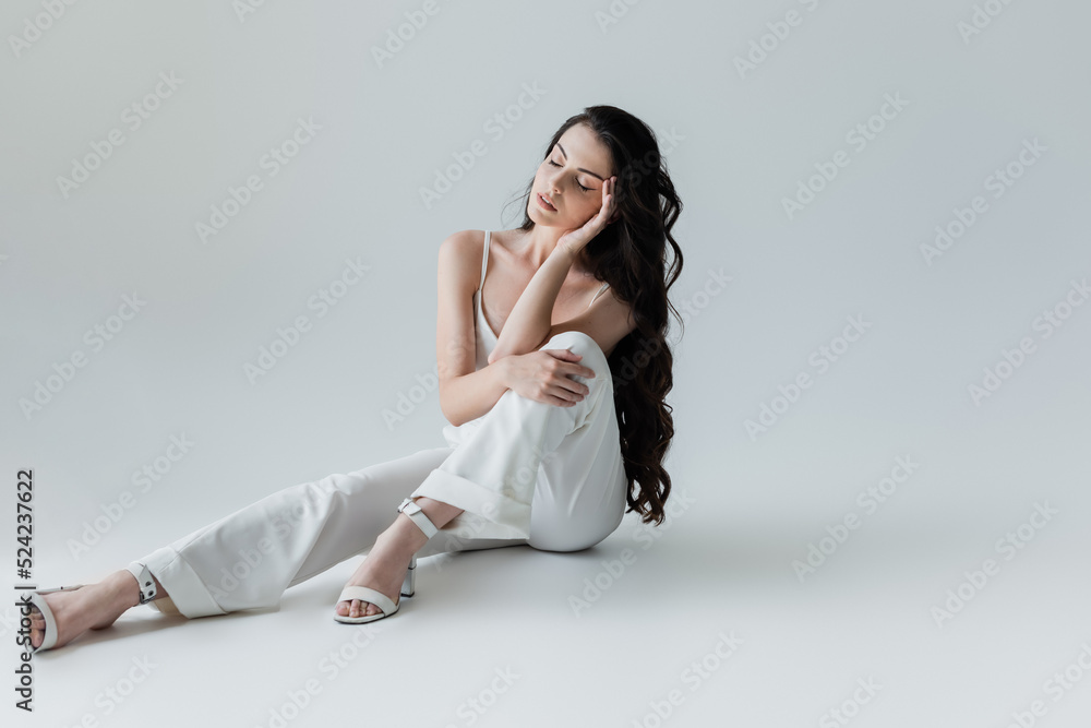Stylish woman in white clothes sitting on grey background. Stylish woman in white clothes sitting on grey background.