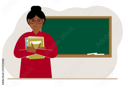 Female teacher with books on the background of the school board.