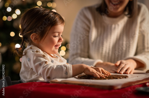 family  cooking and winter holidays concept - happy mother and baby daughter having fun with dough for gingerbread cookies at home on christmas