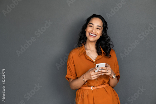 Laughing happy smiling woman messaging on mobile phone on gray wall