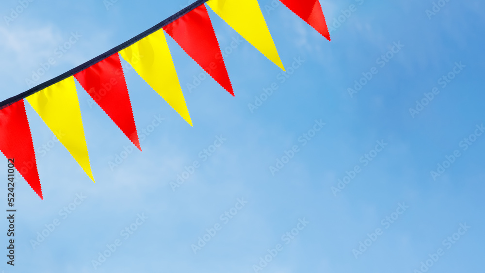 Festive ribbon of red and yellow triangle flags on the white clouds and blue sky background Festive ribbon of red and yellow triangle flags on the white clouds and blue sky background