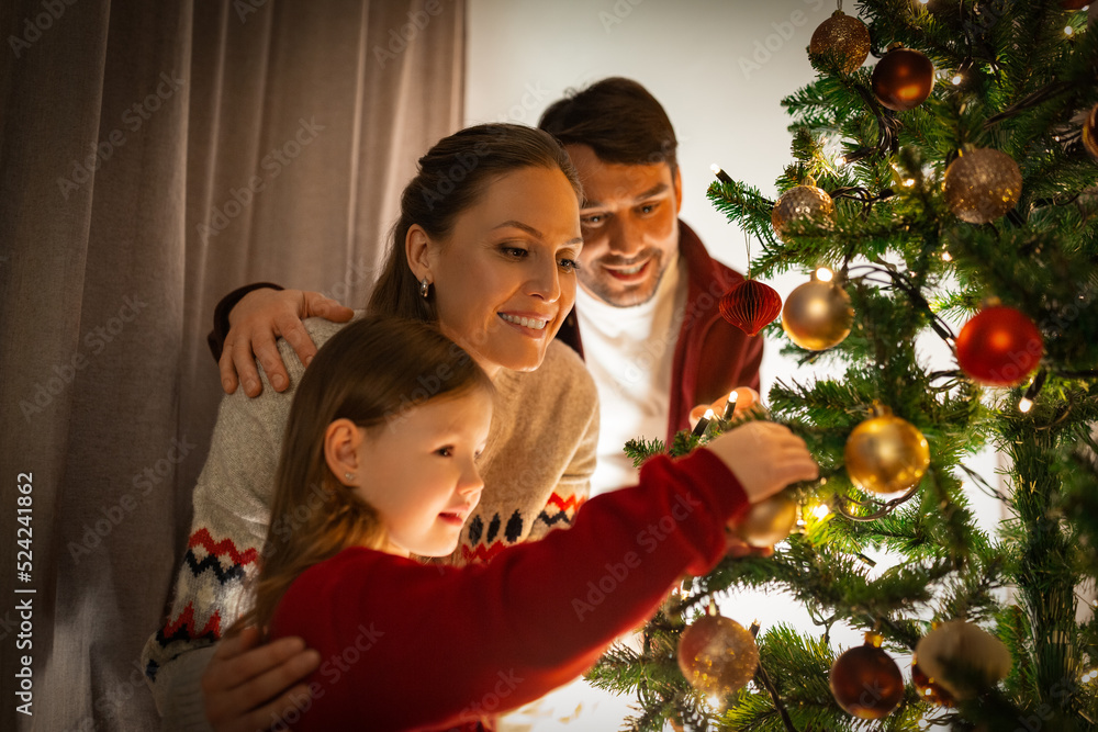 family, winter holidays and people concept - happy mother, father and little daughter decorating christmas tree at home