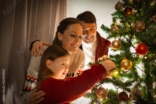 family, winter holidays and people concept - happy mother, father and little daughter decorating christmas tree at home