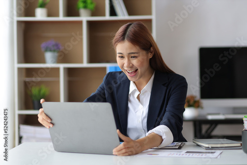 Businesswoman in office looking at laptop screen and showing excitement and joy about a successful business project.