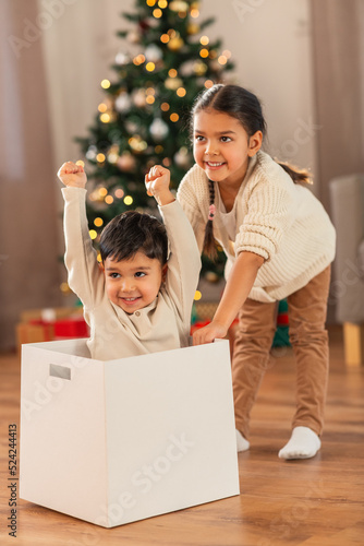 christmas, winter holidays and childhood concept - happy little girl and boy playing with box at home