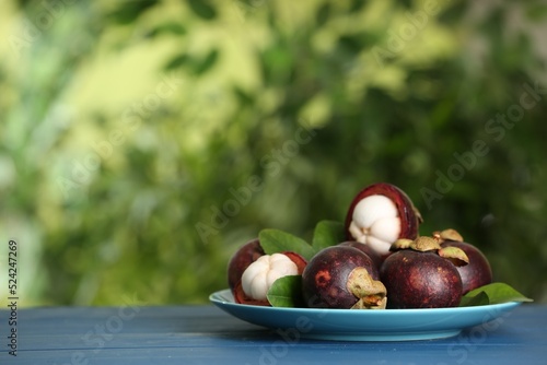 Delicious ripe mangosteen fruits on blue wooden table outdoors, space for text