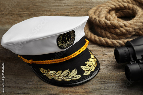 Peaked cap, rope and binoculars on wooden background