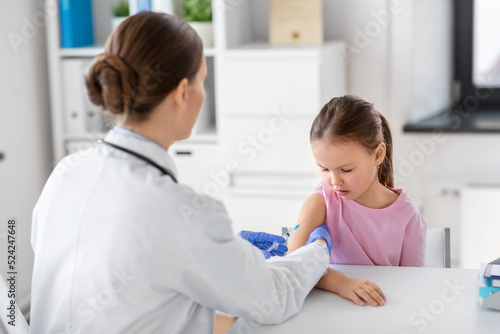 medicine  healthcare and vaccination concept - female doctor or pediatrician with syringe making vaccine injection to little girl patient at clinic