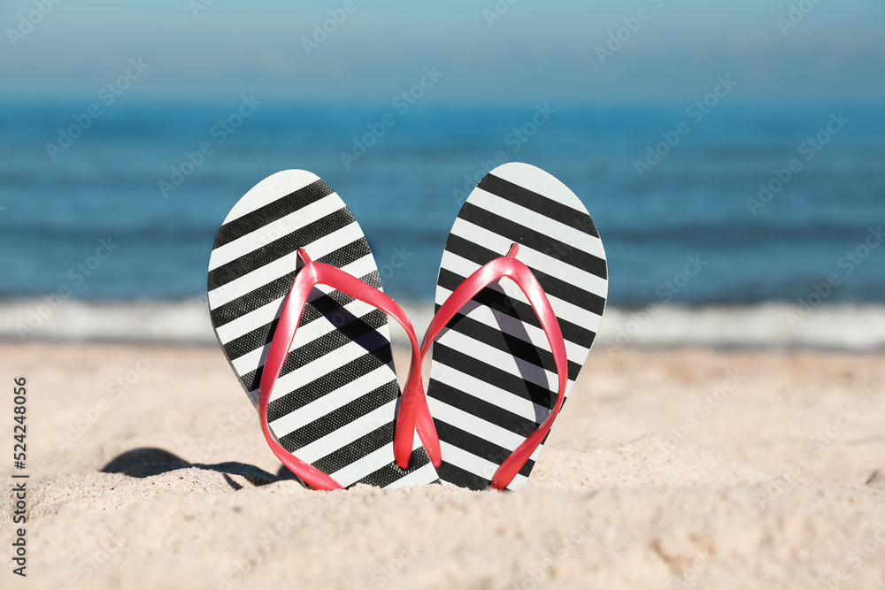 Striped flip flops in sand on beach near sea Striped flip flops in sand on beach near sea