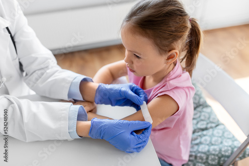 medicine, healthcare and vaccination concept - female doctor or pediatrician attaching medical patch to little girl patient's hand at clinic