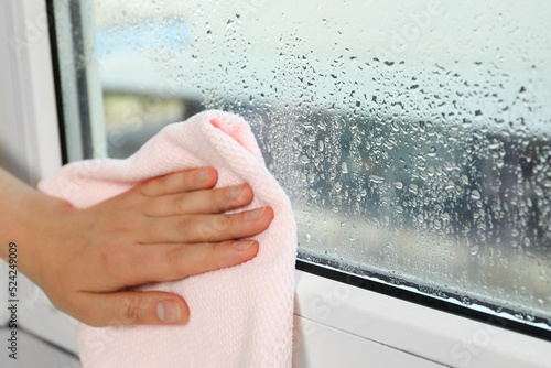 Woman wiping window glass with drops of condensate indoors, closeup. Space for text photo
