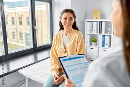 medicine, healthcare and people concept - female doctor with clipboard talking to smiling woman patient at hospital