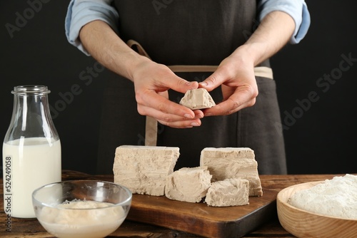 Woman with compressed yeast and dough ingredients at wooden table, closeup