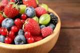 Mix of ripe berries in wooden bowl on table, closeup
