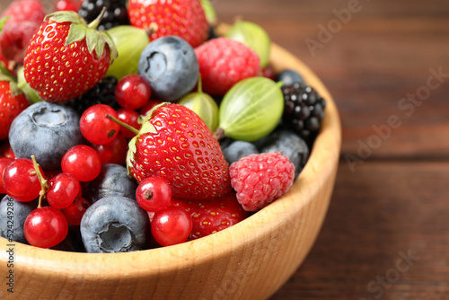 Mix of ripe berries in wooden bowl on table  closeup