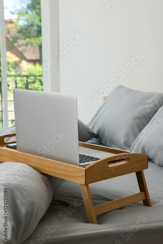 Wooden tray table with laptop on bed indoors