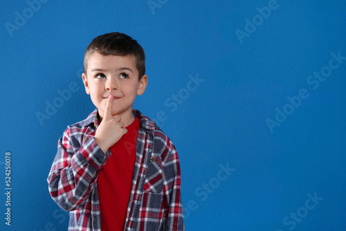 Thoughtful little boy on blue background, space for text